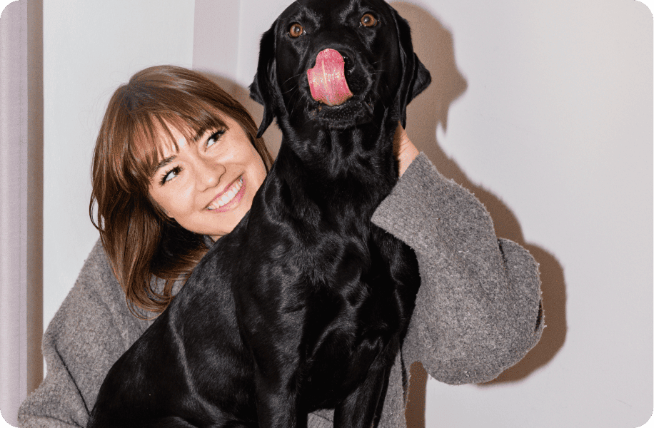 Frau umarmt lachend ihren Labrador, der die Zunge herausstreckt